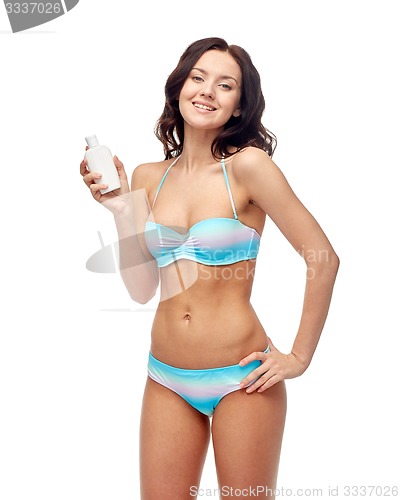 Image of happy young woman in swimsuit holding sunscreen