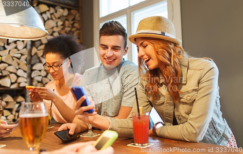 Image of happy friends with smartphones and drinks at bar