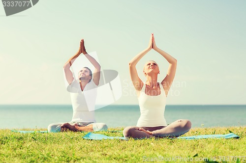Image of smiling couple making yoga exercises outdoors