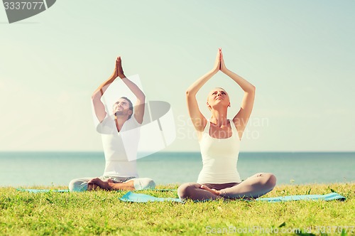 Image of smiling couple making yoga exercises outdoors
