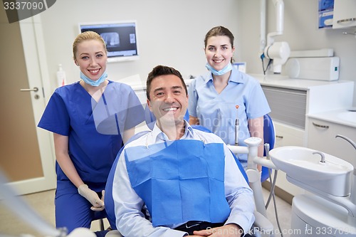 Image of happy female dentists with man patient at clinic