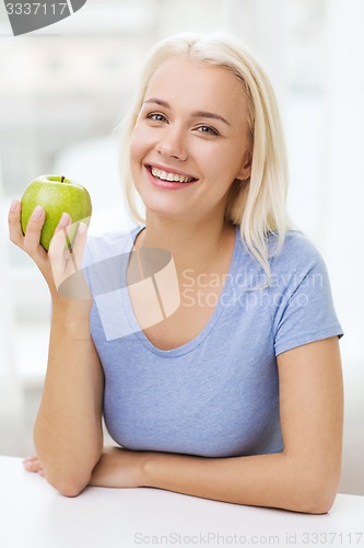 Image of happy woman eating green apple at home