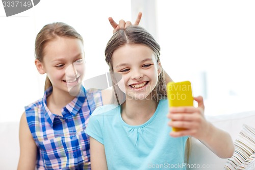 Image of happy girls with smartphone taking selfie at home