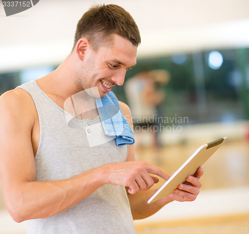 Image of young man with tablet pc computer and towel in gym
