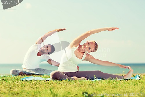 Image of smiling couple making yoga exercises outdoors