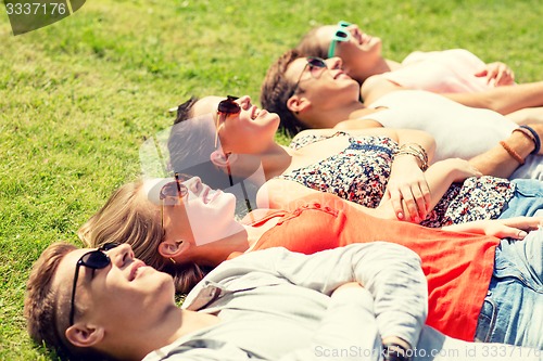 Image of group of smiling friends lying on grass outdoors