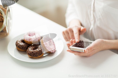 Image of close up of hands with smart phone and donuts