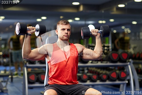 Image of young man with dumbbells flexing muscles in gym