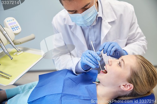 Image of male dentist in mask checking female patient teeth