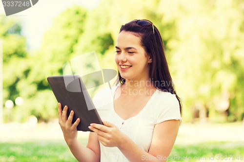 Image of smiling young girl with tablet pc sitting on grass