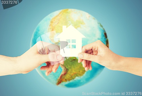 Image of couple hands holding green house over earth globe