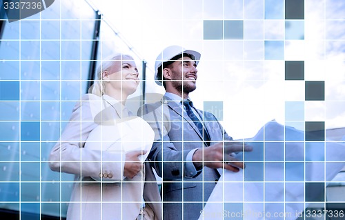 Image of smiling business people in helmets with blueprint