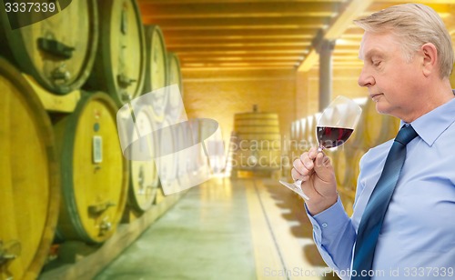 Image of senior man smelling red wine in cellar