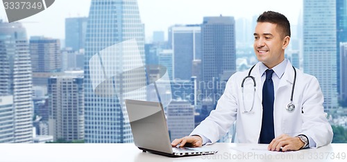 Image of smiling male doctor with laptop sitting at table