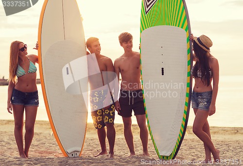 Image of smiling friends in sunglasses with surfs on beach