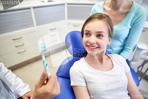 Image of happy dentist showing toothbrush to patient girl