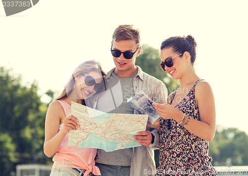 Image of smiling friends with map and city guide outdoors