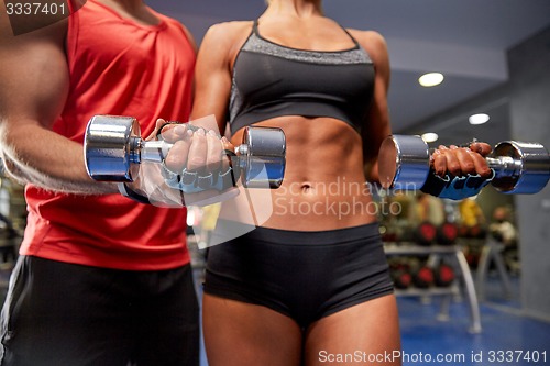 Image of young couple with dumbbell flexing muscles in gym