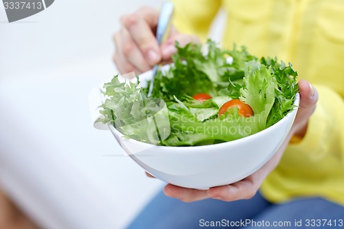 Image of close up of young woman eating salad at home