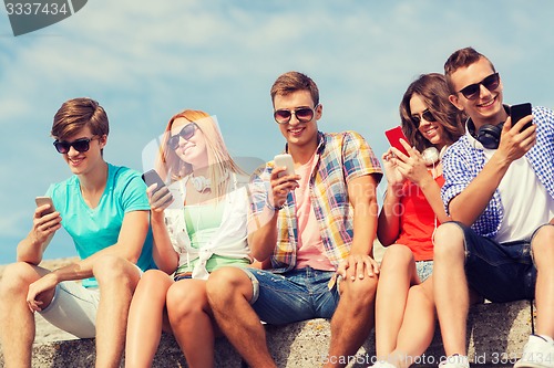 Image of group of smiling friends with smartphones outdoors