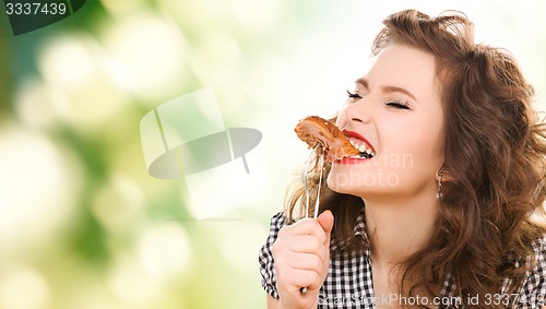 Image of hungry young woman eating meat on fork over green