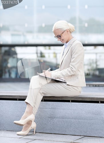 Image of young smiling businesswoman with notepad outdoors