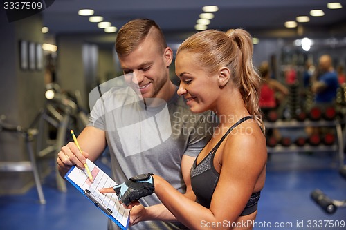 Image of smiling woman with trainer and clipboard in gym