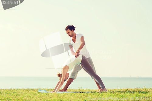 Image of smiling couple making yoga exercises outdoors