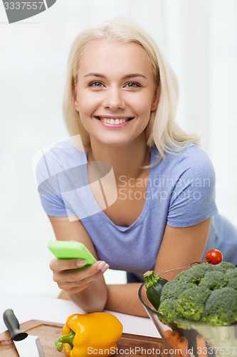 Image of smiling woman with smartphone cooking vegetables