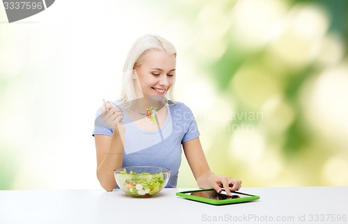 Image of smiling woman eating salad with tablet pc