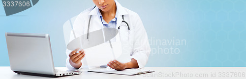 Image of female doctor with laptop pc looking at paper