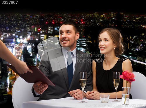 Image of waiter giving menu to happy couple at restaurant