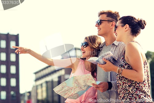 Image of smiling friends with map and city guide outdoors