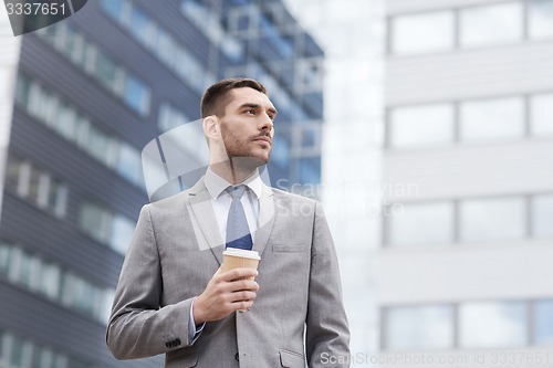 Image of young serious businessman with paper cup outdoors