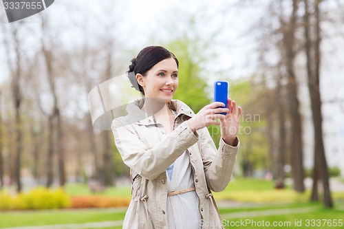 Image of smiling woman taking picture with smartphone