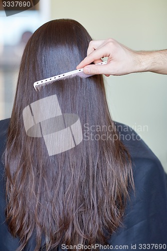 Image of hand with comb combing woman hair at salon