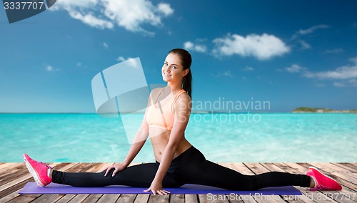 Image of smiling woman doing splits on mat over sea