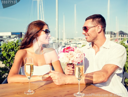 Image of smiling couple with bunch and champagne at cafe