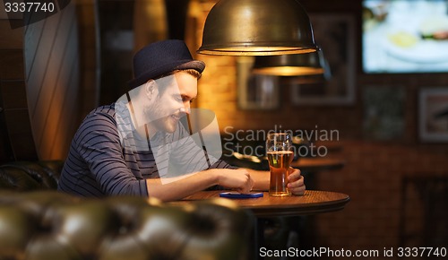 Image of man with smartphone and beer texting at bar