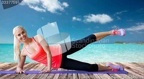 Image of smiling woman exercising on mat over sea