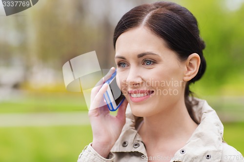 Image of smiling woman calling on smartphone in park