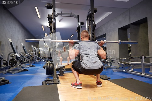 Image of young man flexing muscles with bar in gym