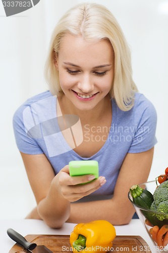 Image of smiling woman with smartphone cooking vegetables