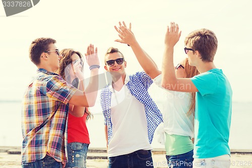 Image of group of smiling friends making high five outdoors