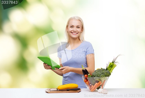 Image of smiling woman with tablet pc cooking vegetables
