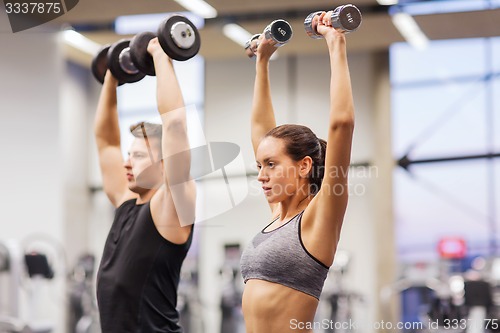 Image of smiling man and woman with dumbbells in gym