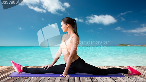 Image of smiling woman doing splits on mat over sea