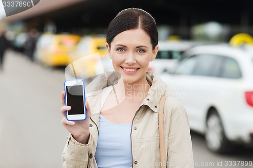 Image of smiling woman showing smartphone over taxi in city