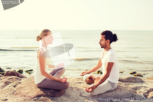 Image of smiling couple making yoga exercises outdoors