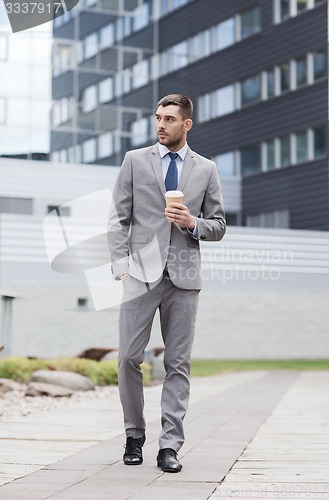Image of young serious businessman with paper cup outdoors